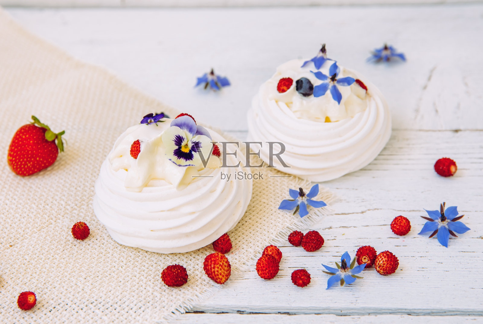 小的蛋白酥饼，用鲜奶油、新鲜浆果和真正的可食用花朵装饰。照片摄影图片