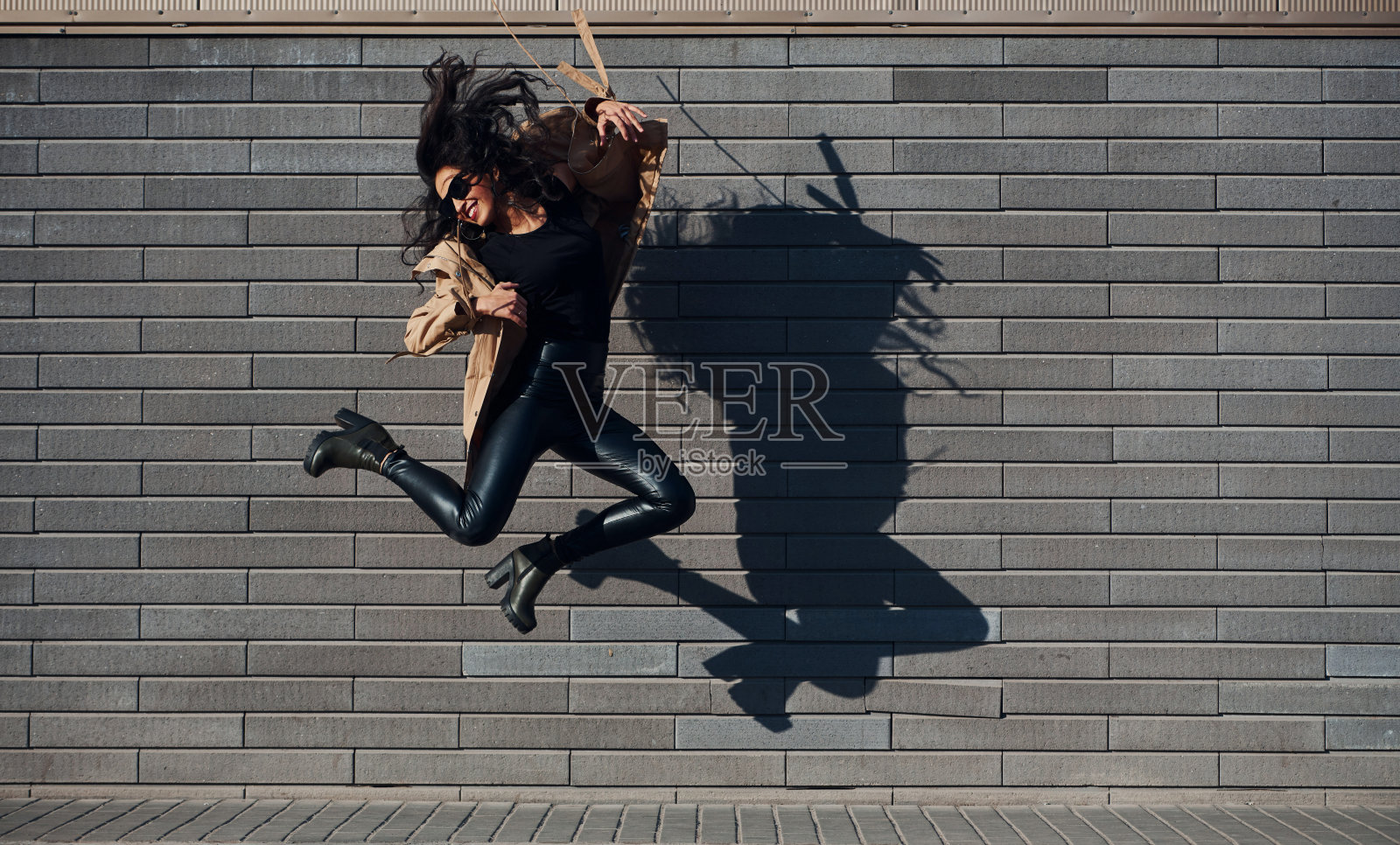 美丽的黑发与卷曲的头发和在黑色的衣服跳和有乐趣的户外靠近墙照片摄影图片