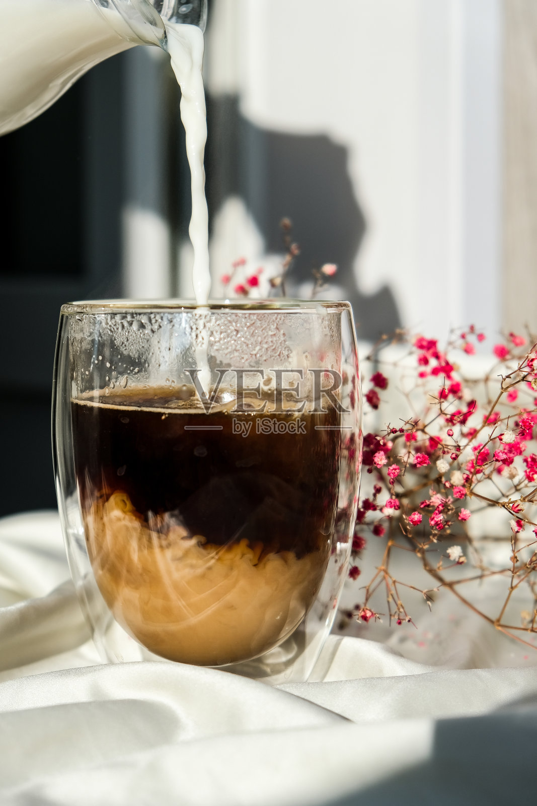 牛奶倒入玻璃杯和黑咖啡。早上美学氛围。早餐。粉色满天星花照片摄影图片