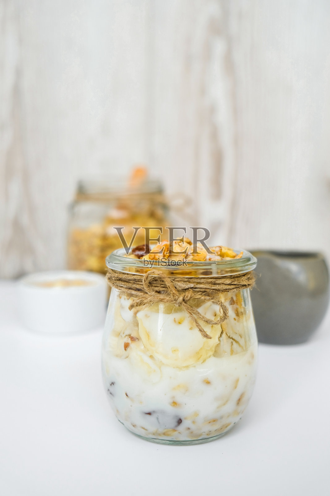 健康的早餐。燕麦格兰诺拉麦片与希腊酸奶和坚果香蕉麦片在罐子里在光线的背景。素食、素食与减肥的饮食概念。排毒菜单照片摄影图片