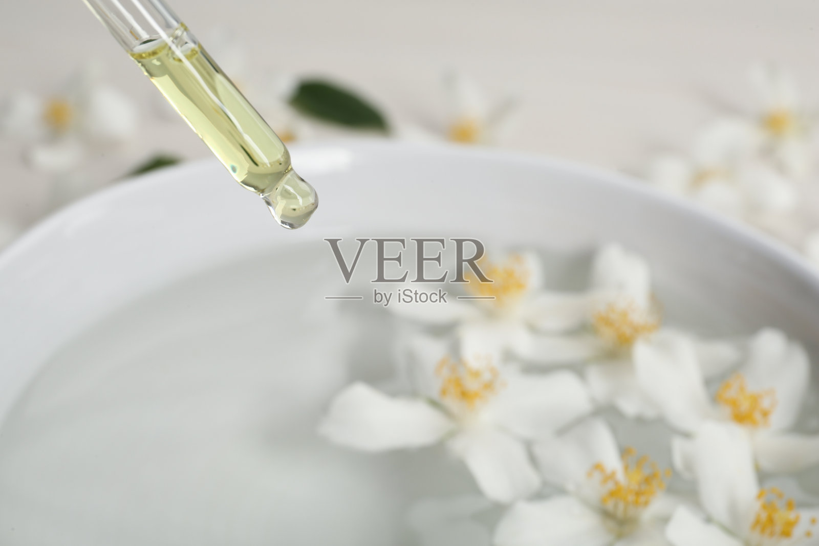 将茉莉精油滴入有花的碗中，特写照片摄影图片