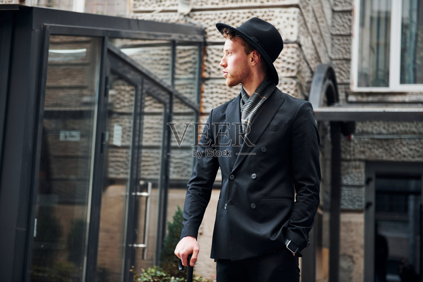 优雅的年轻人戴着黑帽子，穿着黑衣服，手里拿着雨伞在城外照片摄影图片