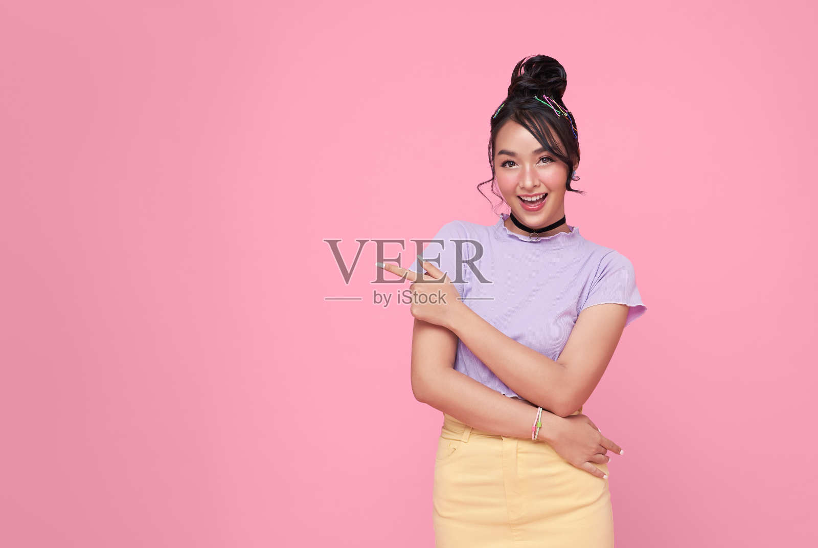 快乐年轻的亚洲少女站在她的手指孤立的粉红色背景与复制空间。照片摄影图片