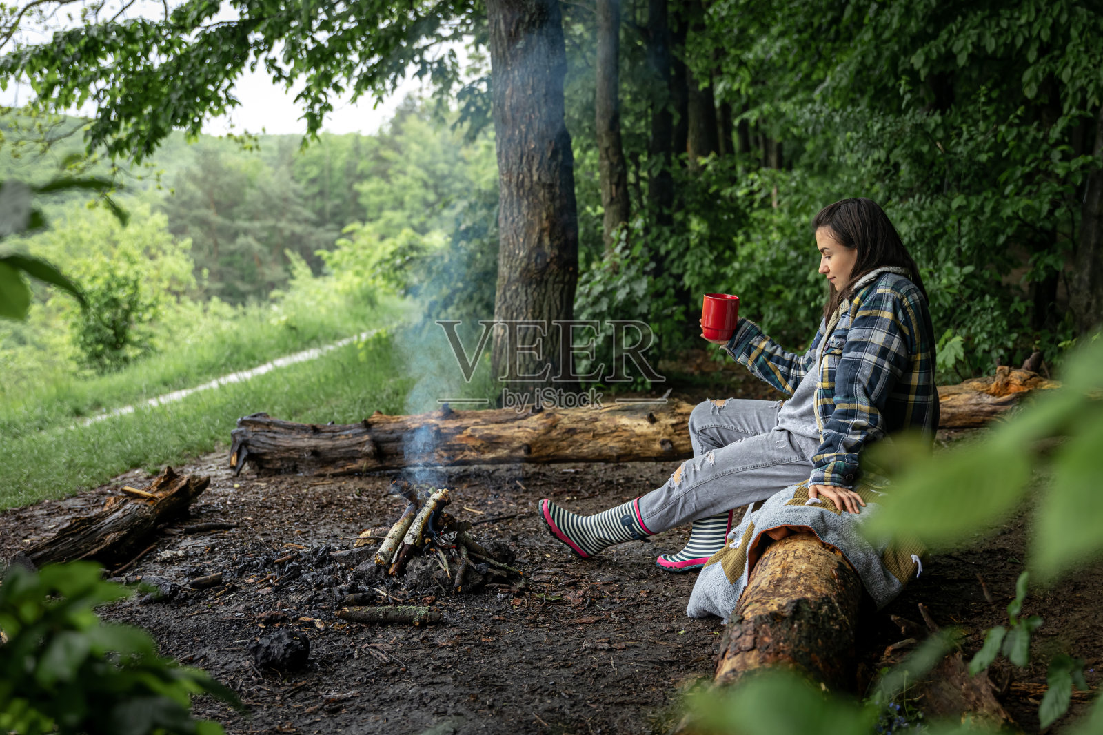 一个迷人的女孩与一个杯子在她的手在森林的火附近温暖。照片摄影图片