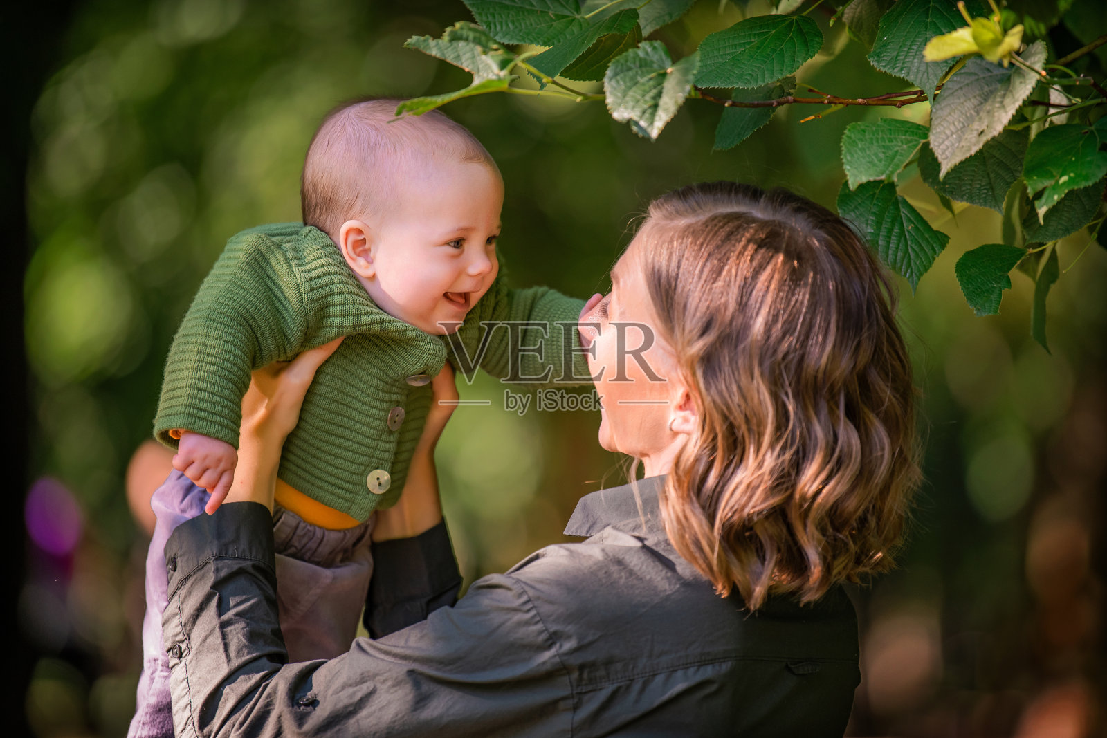 一个快乐的年轻母亲的肖像在她的胳膊半岁的婴儿在夏天在公园的户外照片摄影图片
