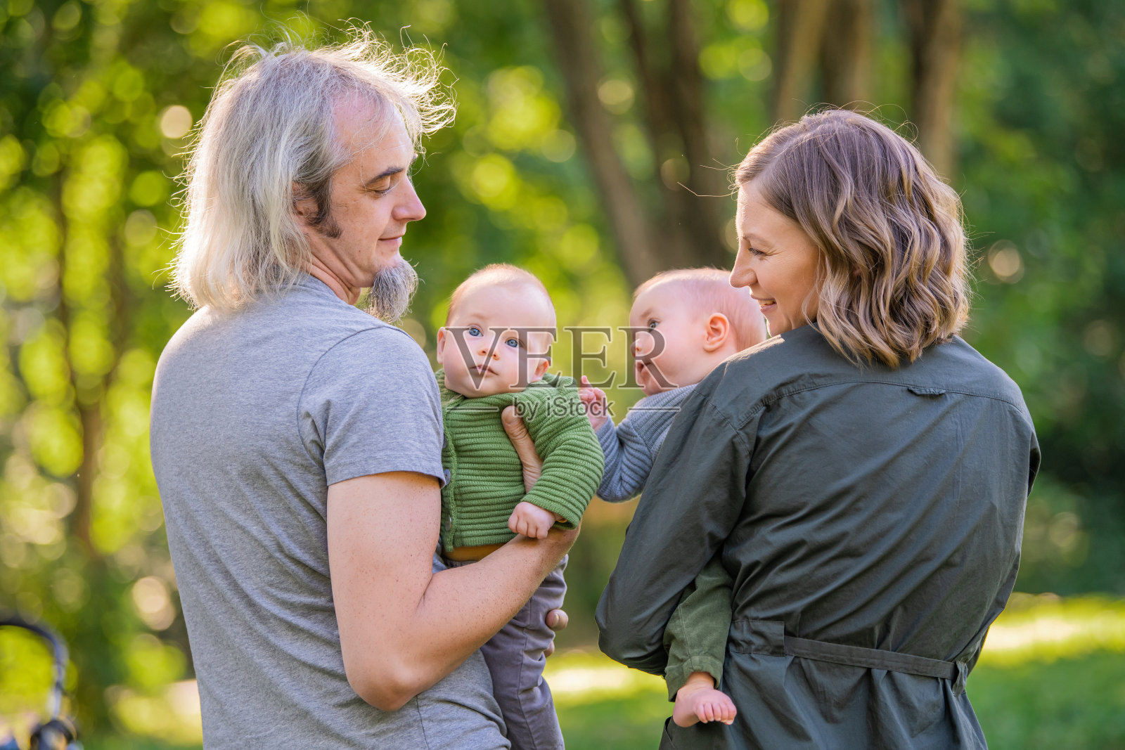 一对幸福的夫妇和一对双胞胎在大自然中休息。以绿色植物为背景的肖像照片摄影图片
