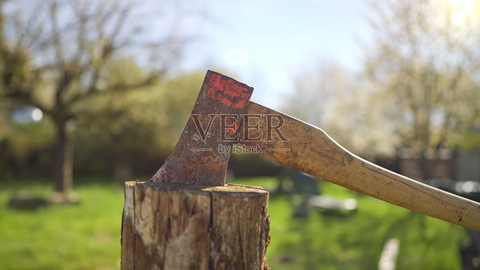 阳光明媚的春日里，一个戴着草帽穿着格子衬衫的男人正在花园里劈柴照片摄影图片