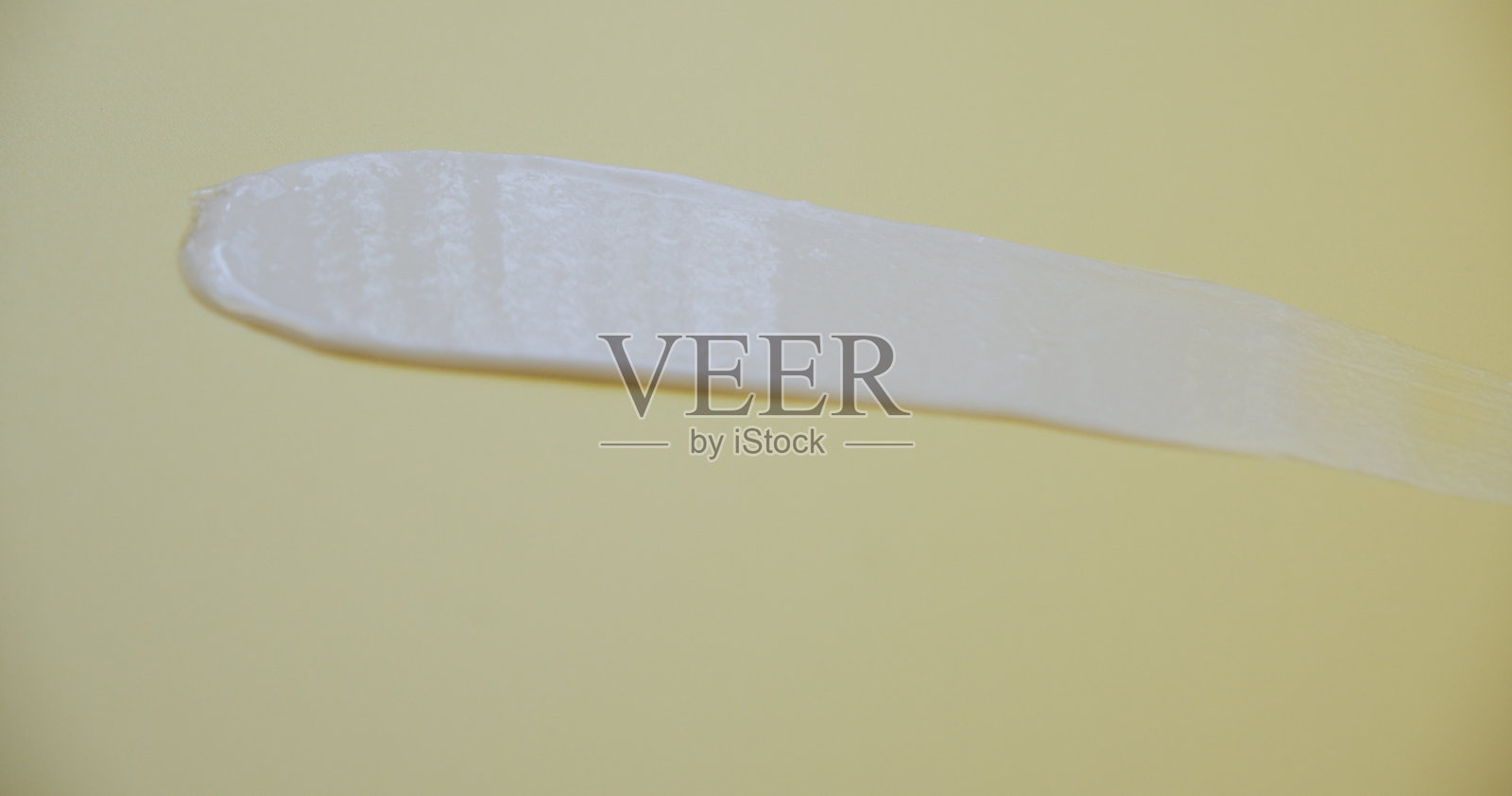 奶油质地。在黄色背景上涂抹白色护手霜。照片摄影图片