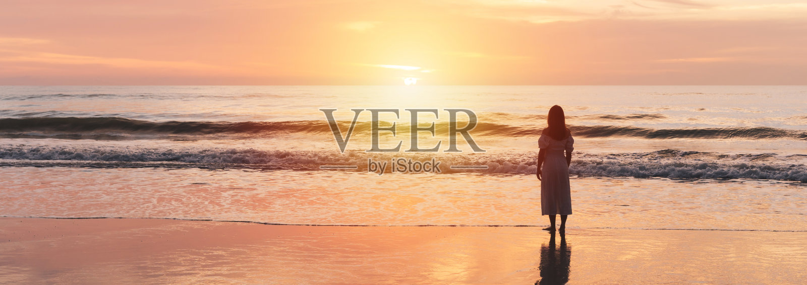 孤独的年轻女子走在宁静的海滩上，享受美丽的日落，在暑假的概念旅行照片摄影图片