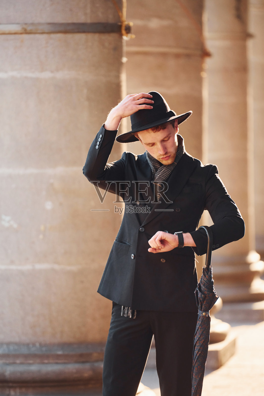 优雅的年轻人戴着黑帽子，穿着黑衣服，手里拿着雨伞在城外照片摄影图片