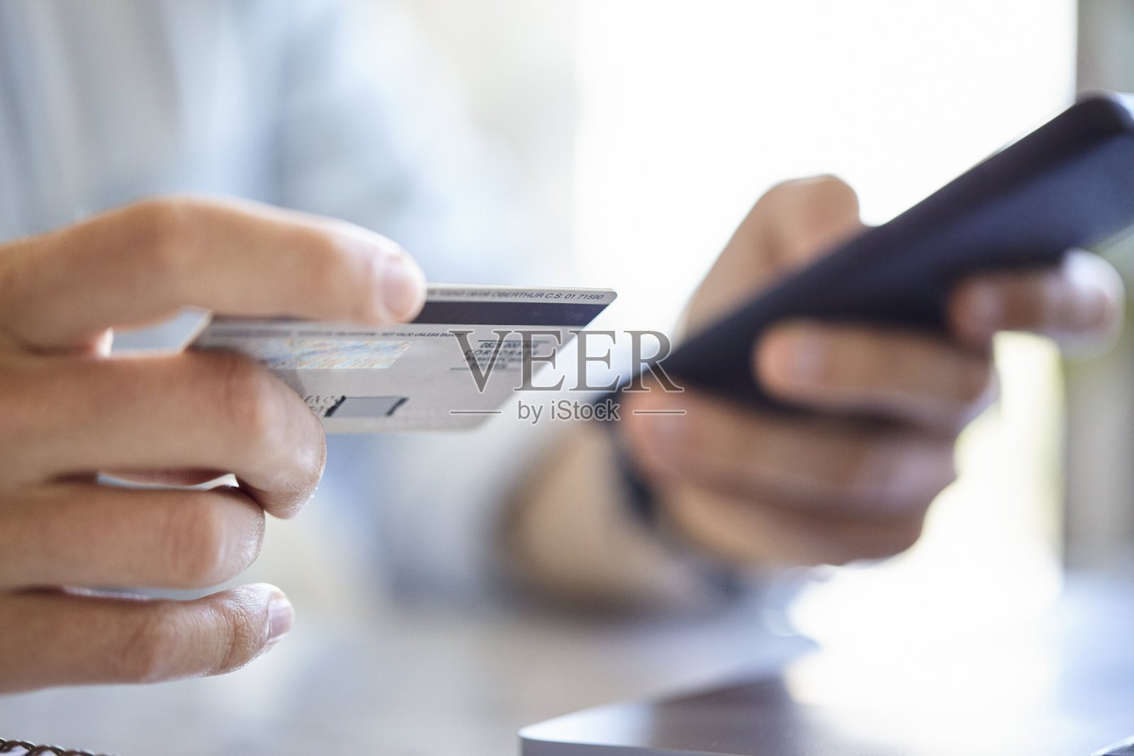 年轻的成年男子持有信用卡，而购买网上使用智能手机在白天照片摄影图片