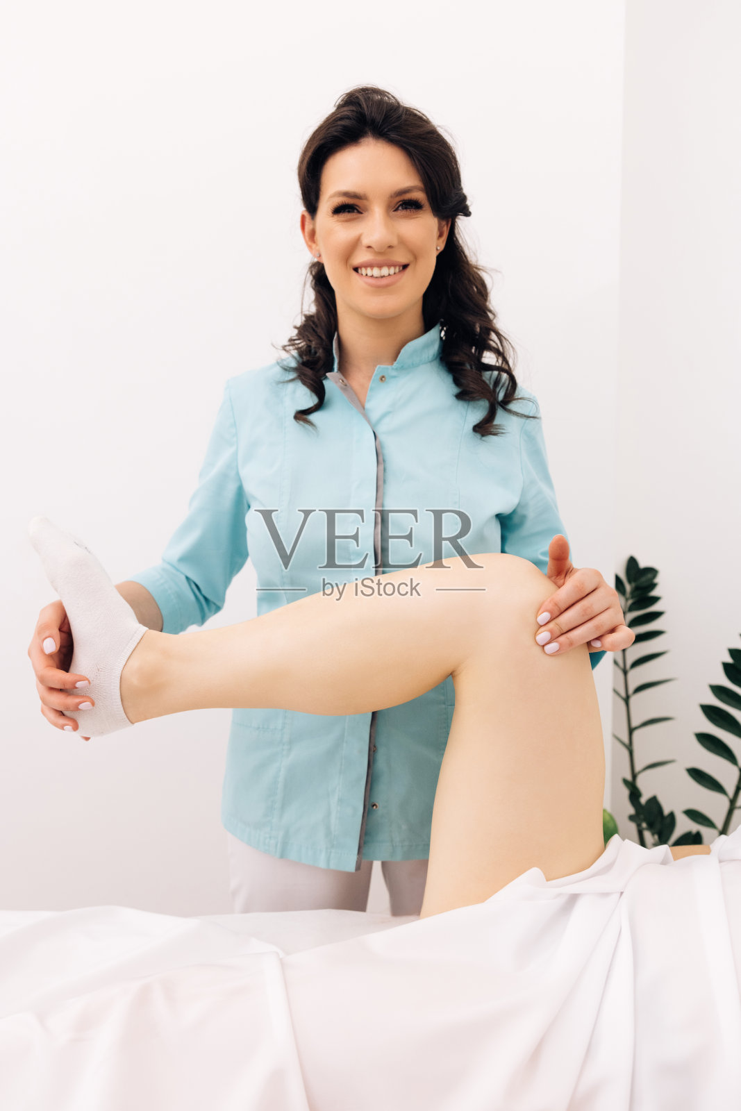 现代康复门诊创伤后康复专业医生。物理治疗师在医院的床上伸展女性病人-物理治疗的概念。医疗保健的概念照片摄影图片