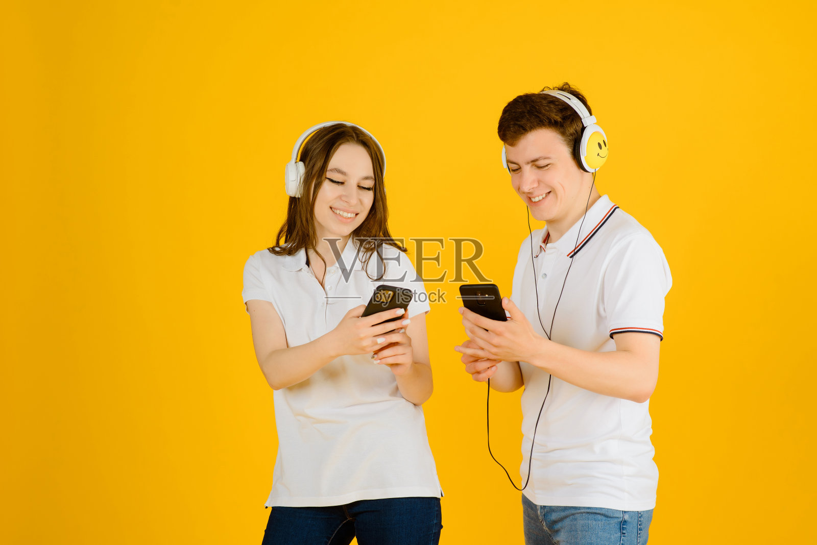 一对年轻幸福的夫妇戴着耳机听音乐，在黄色背景下大笑。照片摄影图片