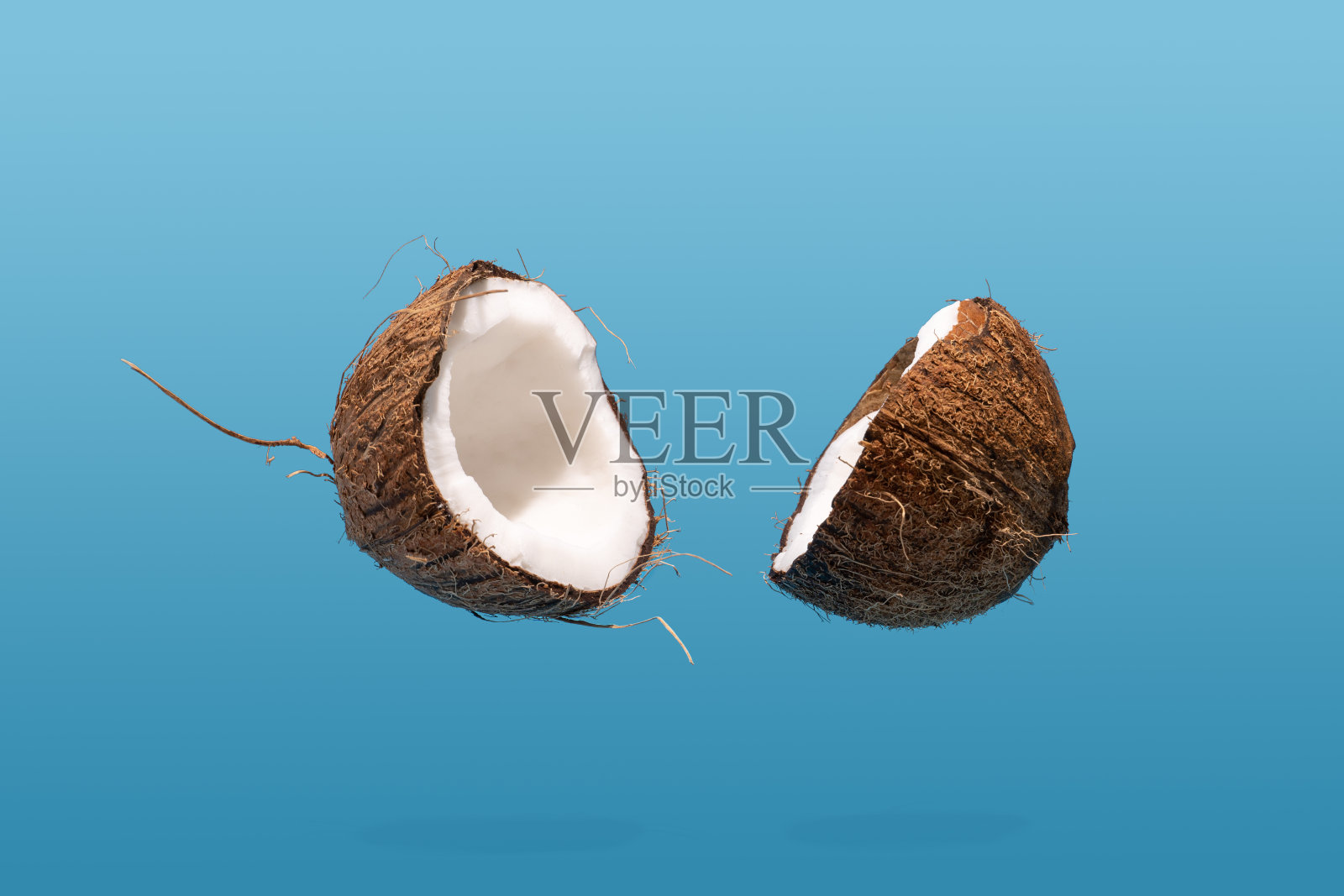 漂浮的椰子在蓝色背景上裂开了一半。创新食品的概念照片摄影图片