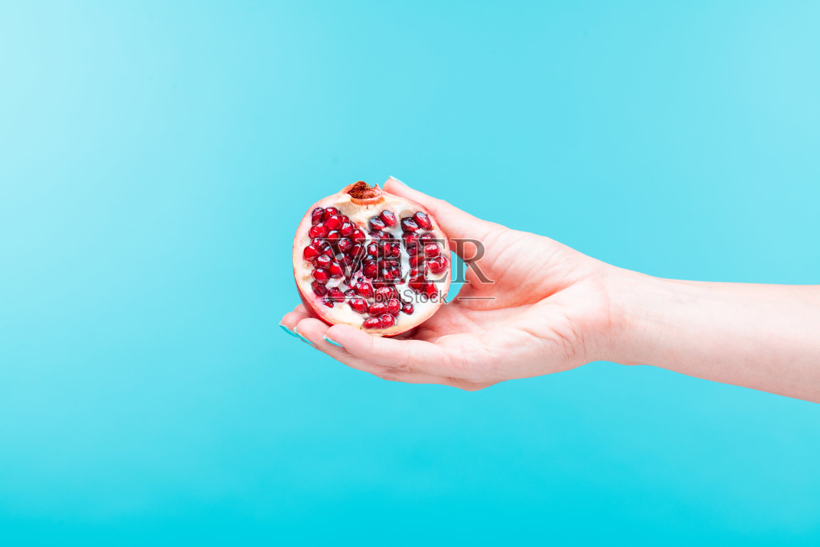 手握石榴在明亮的蓝色背景。照片摄影图片
