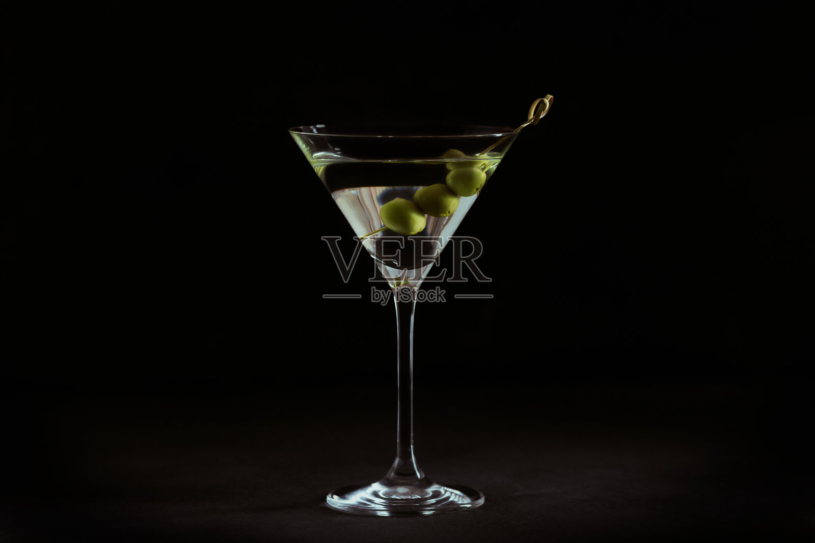 一杯经典的干马提尼鸡尾酒和橄榄放在黑色的石头桌子上。照片摄影图片