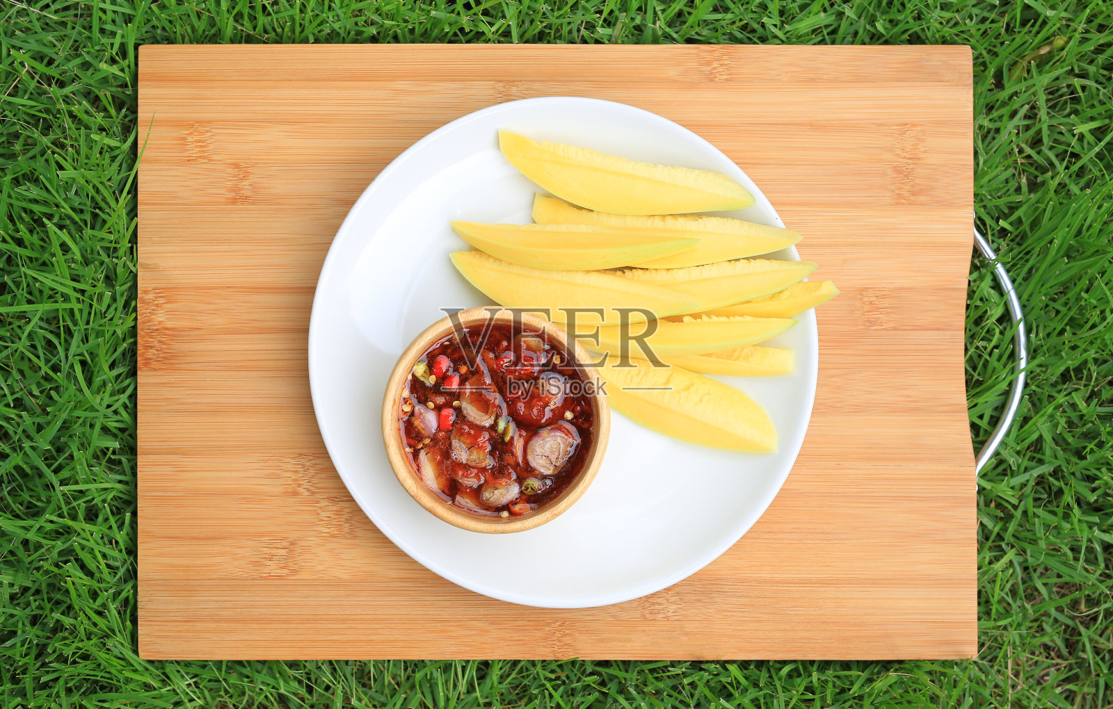 白盘子里的芒果酸鱼和甜鱼酱放在竹木板上，以绿草为背景。俯视图照片摄影图片