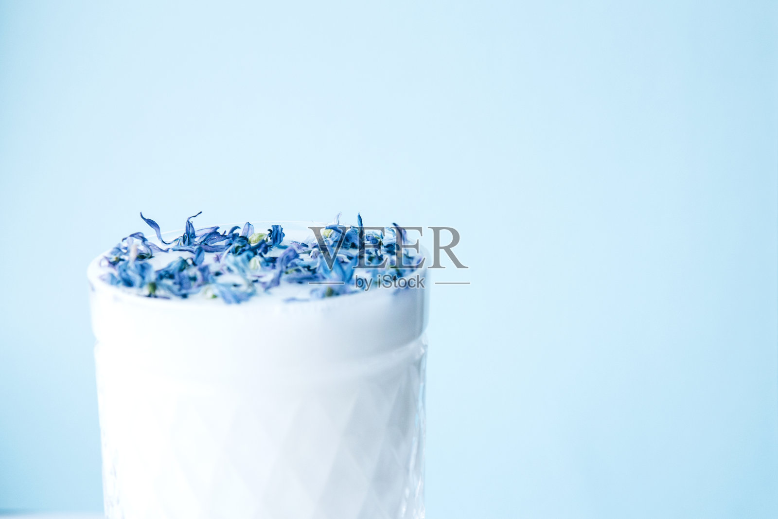 蓝色背景上的牛奶和蓝色花瓣的水晶玻璃。花在牛奶照片摄影图片