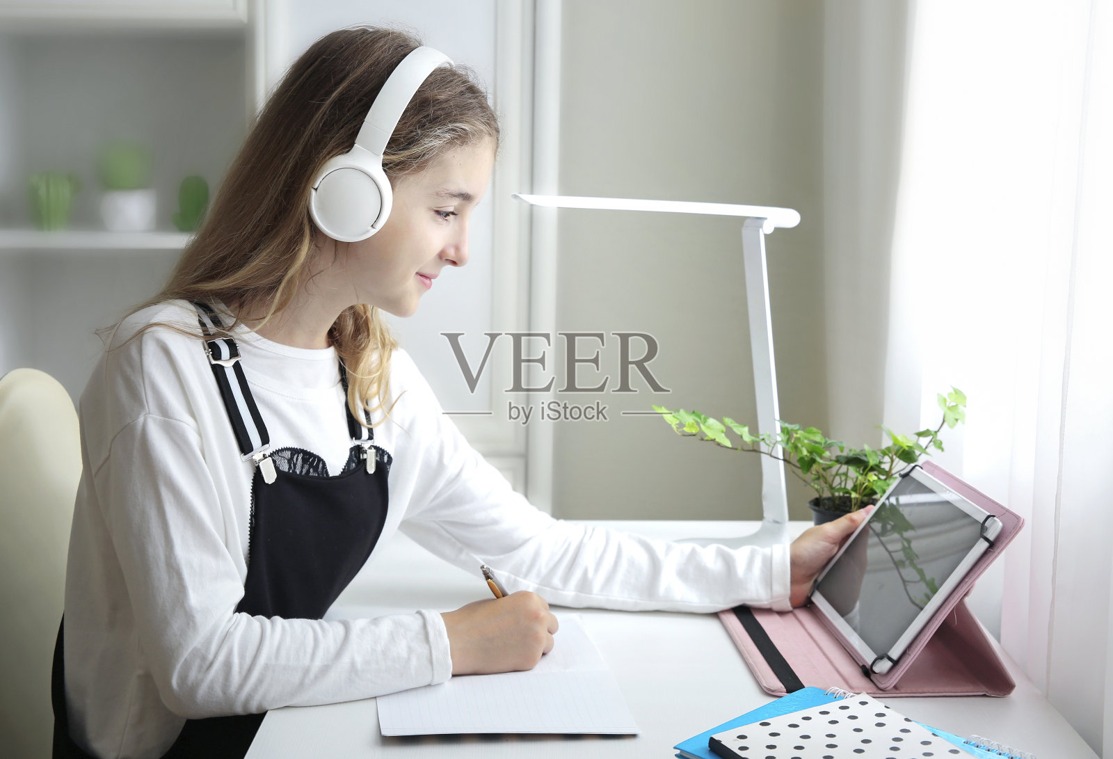 小女孩坐在桌子旁，带着平板电脑和耳机学习。在线educattion回家。学校隔离放大。学生学习。照片摄影图片