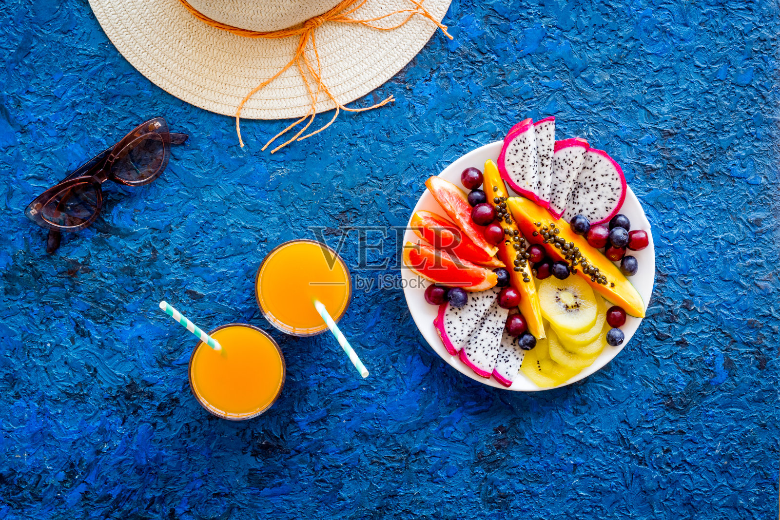 度假热带水果早餐。水果与新鲜的果汁和帽子，俯视图照片摄影图片
