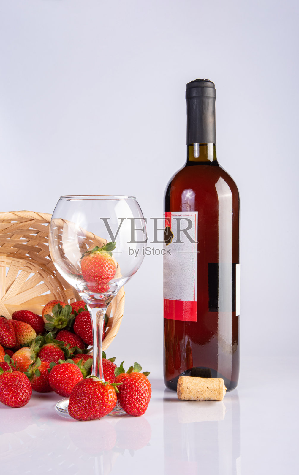 玫瑰葡萄酒瓶和一个水晶玻璃连同美丽的草莓在白色的表面，选择性的焦点。照片摄影图片