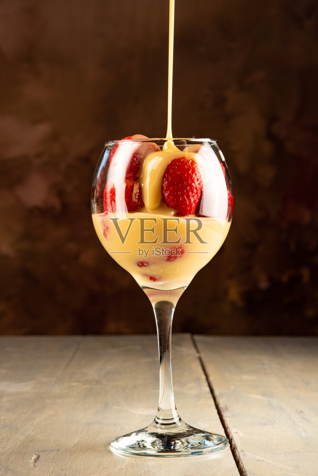 草莓，一碗草莓和炼乳放在旧的白色桌子上，黑色抽象的背景，选择性的焦点。照片摄影图片