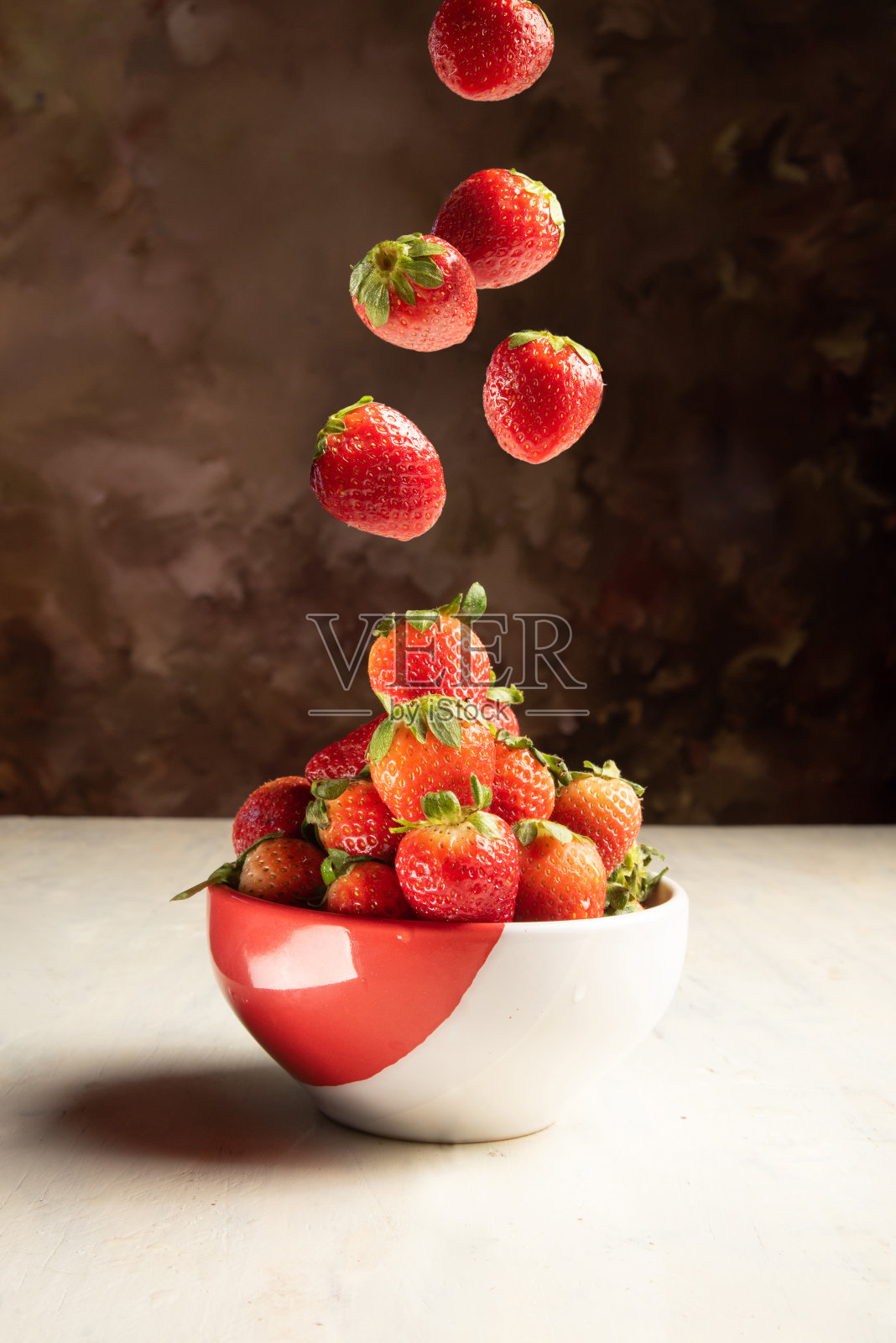 草莓，草莓掉进一个旧的白色桌子上的碗里，黑色抽象的背景，选择性的焦点。照片摄影图片