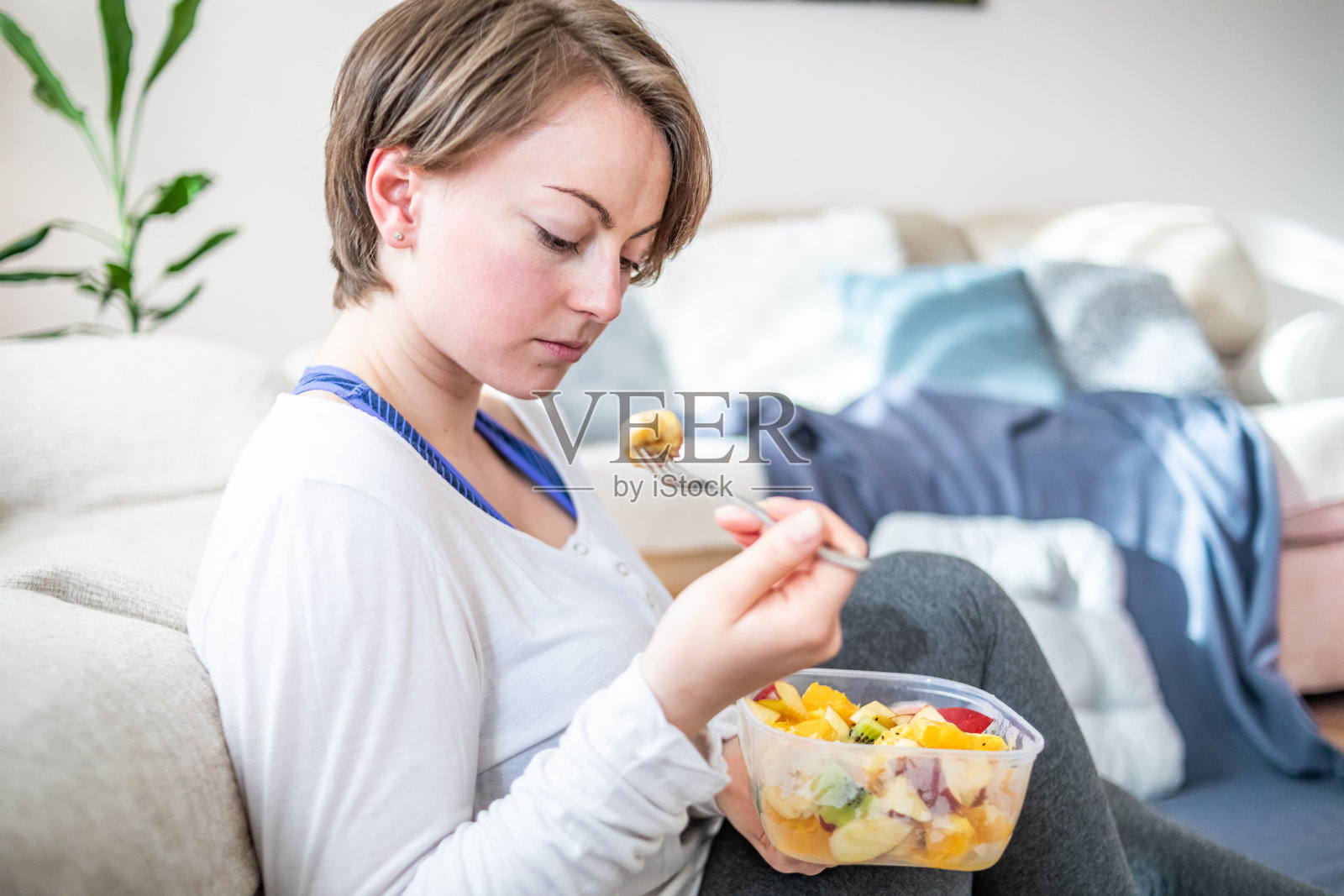 一个女人从一个盘子碗里吃健康的水果沙拉。时刻与塑料照片摄影图片