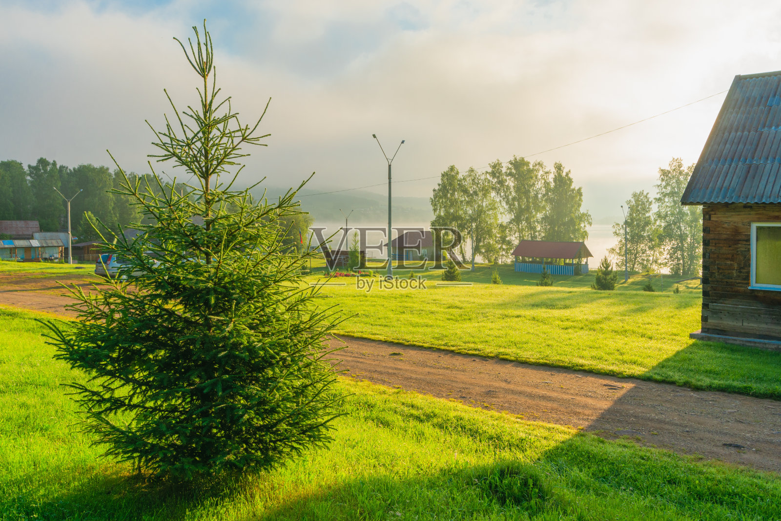 美丽的夏季乡村景观。清晨，太阳照亮了树和小村庄的建筑照片摄影图片