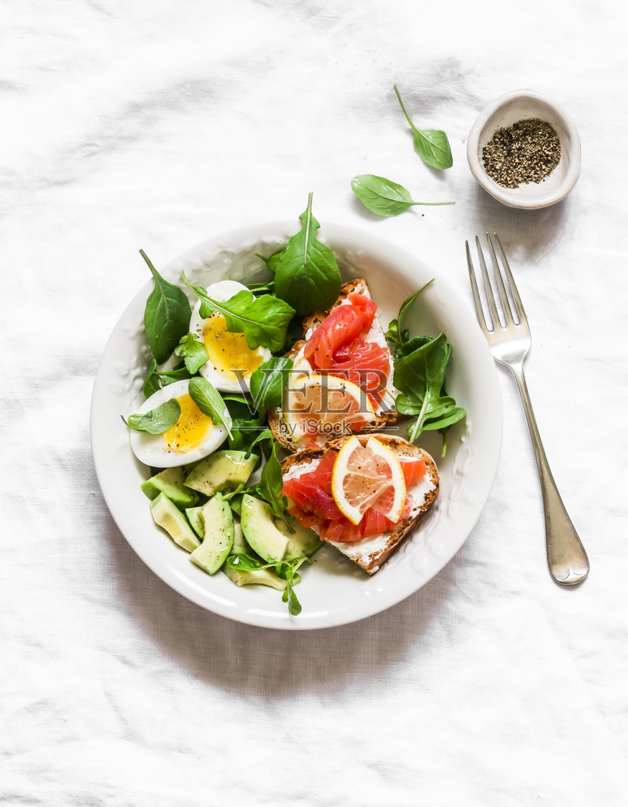 一碗绿色沙拉，牛油果，煮鸡蛋和三明治，黑麦面包，奶油奶酪和鲑鱼在一个较轻的背景，俯视图。美味健康的早餐，早午餐照片摄影图片