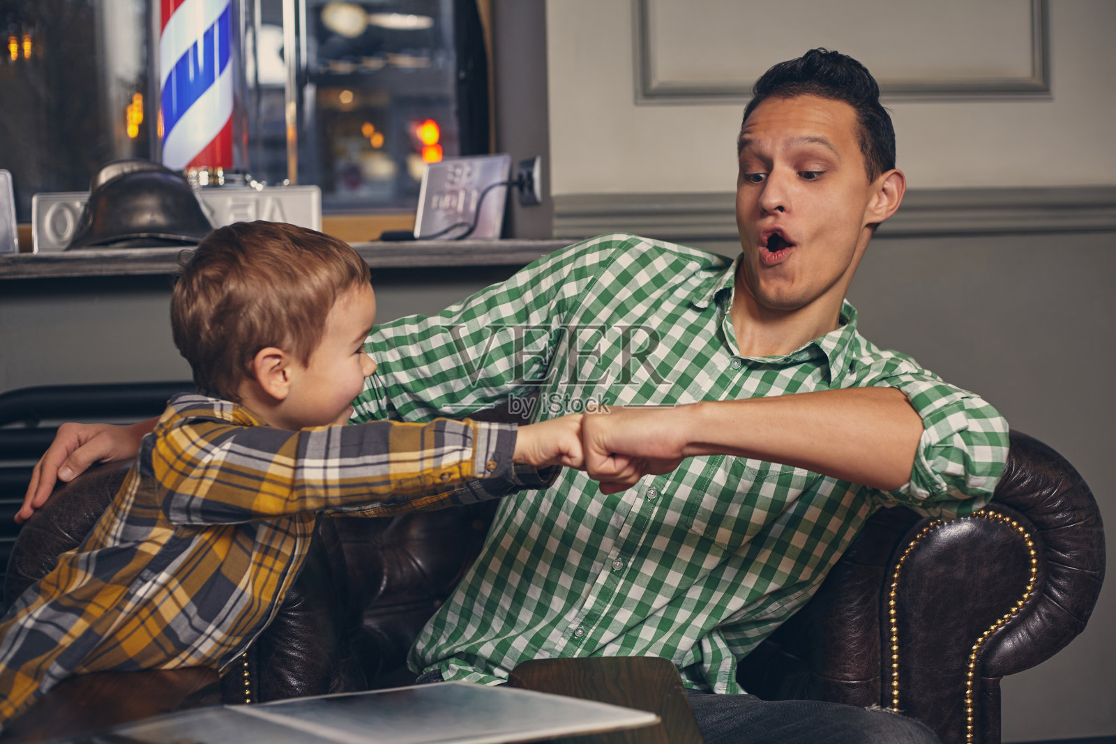 年轻的父亲和他时髦的小儿子在候车室里的理发店里照片摄影图片