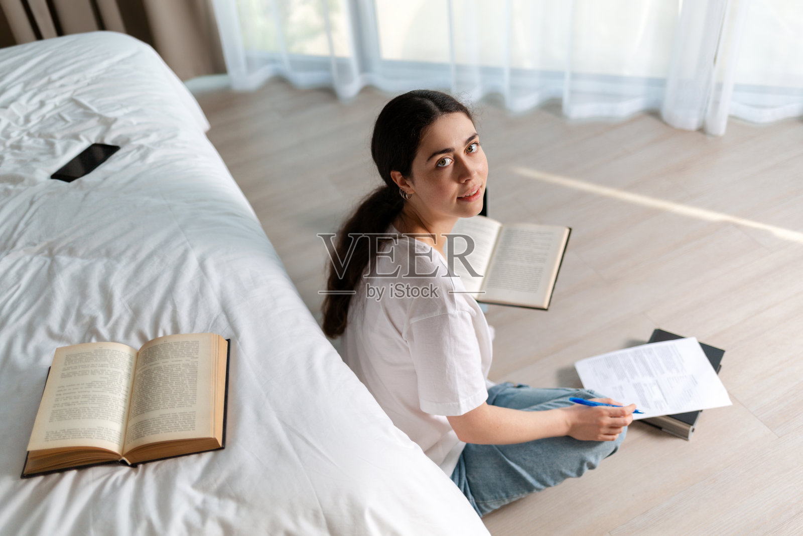 一个年轻漂亮的女人坐在地板上看书。书躺在床上。网络课程和网络教育的概念。俯视图照片摄影图片