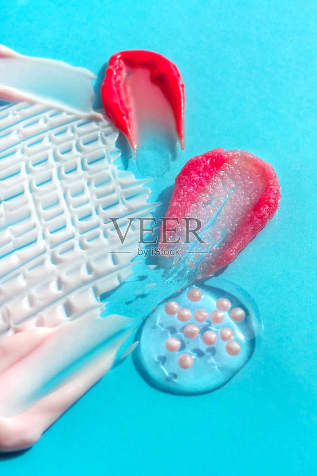 白色和粉红色化妆品涂抹在蓝色的背景。奶油，凝胶，口红，唇彩样本。液体彩妆照片摄影图片