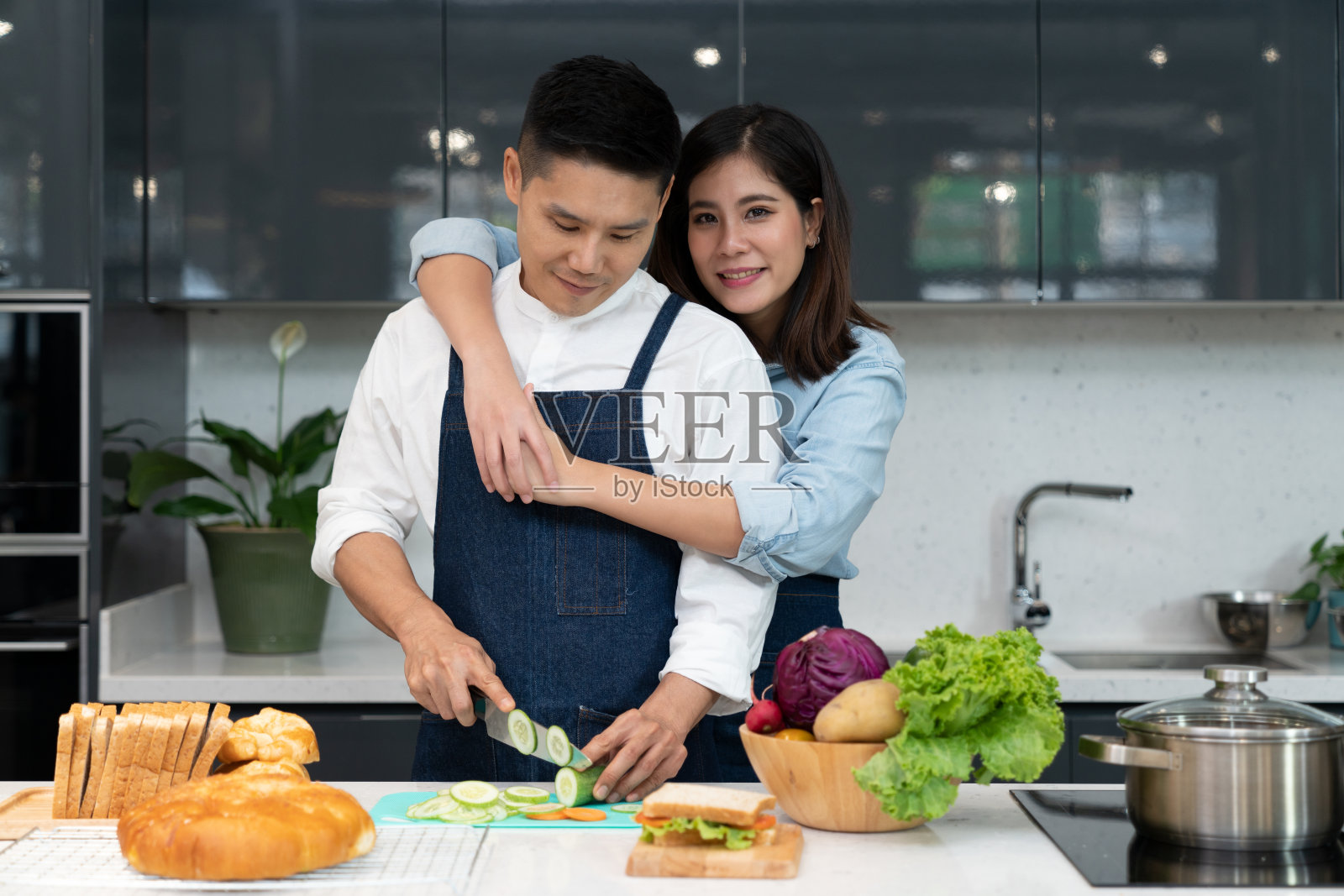 一个快乐的男人和一个年轻的女人在厨房岛上切蔬菜做健康的三明治照片摄影图片