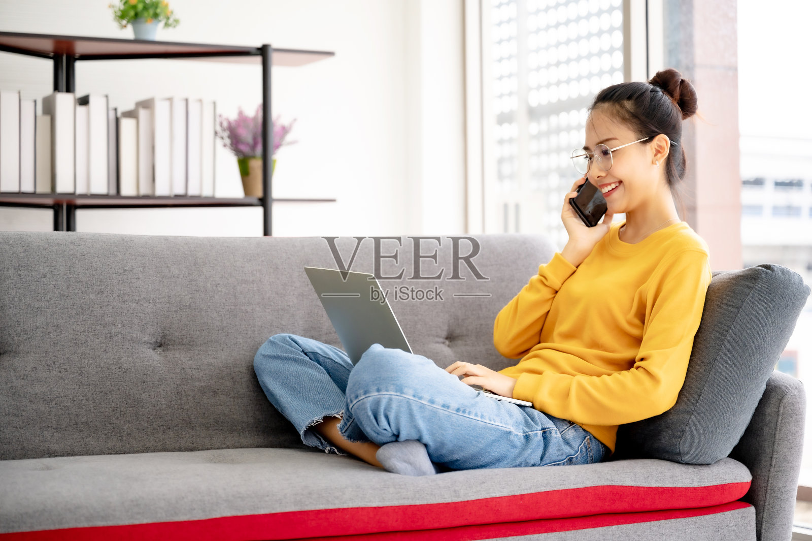 亚洲女人戴眼镜感觉快乐和大大的微笑。她在客厅的沙发上使用电脑、笔记本电脑和手机照片摄影图片