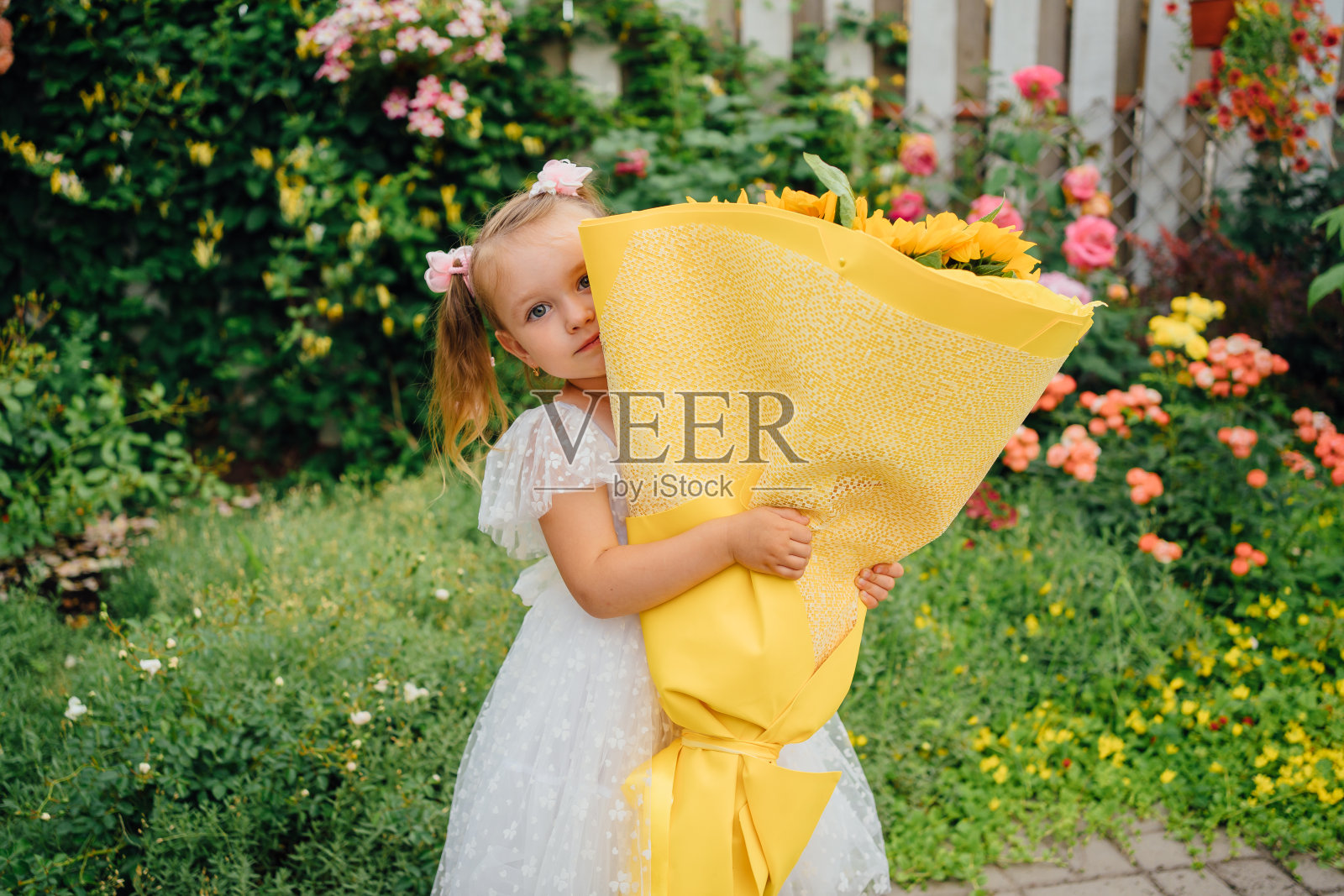 小女孩穿着白色连衣裙，手里捧着一大束黄色的向日葵照片摄影图片