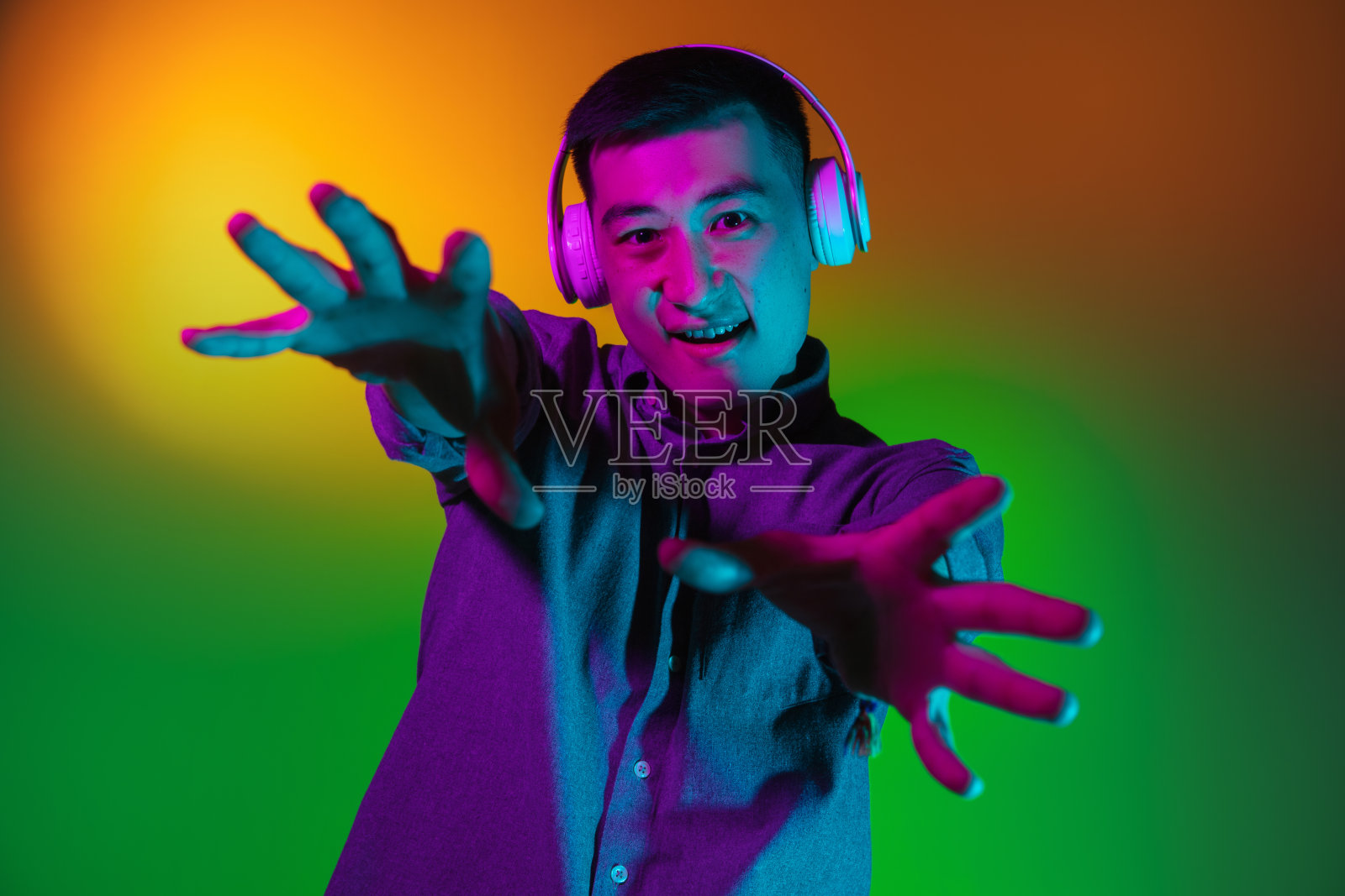 亚洲青年男子的肖像孤立在演播室背景在梯度黄绿色霓虹灯，彩色滤镜。人类情感的概念，面部表情。照片摄影图片