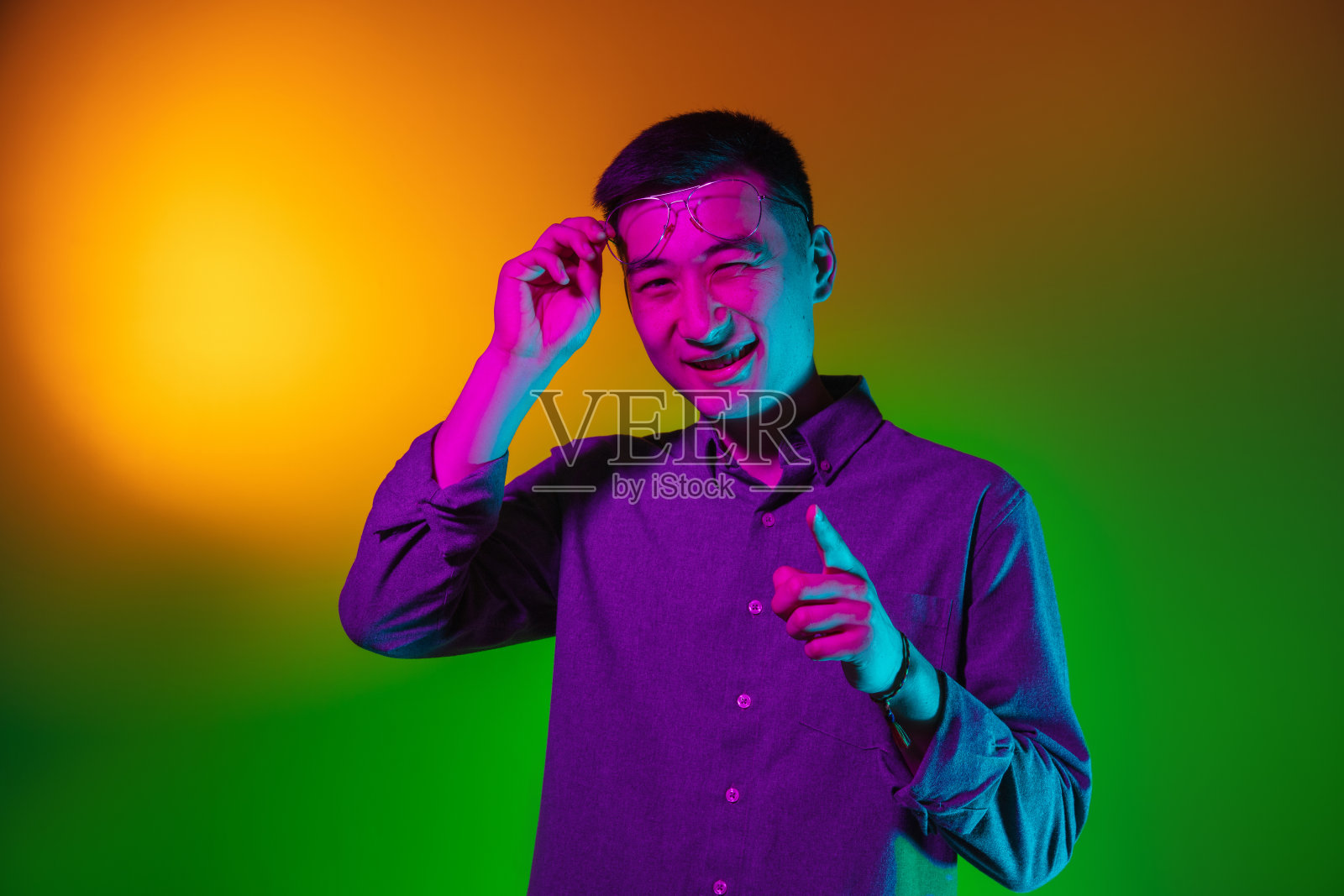 亚洲青年男子的肖像孤立在演播室背景在梯度黄绿色霓虹灯，彩色滤镜。人类情感的概念，面部表情。照片摄影图片