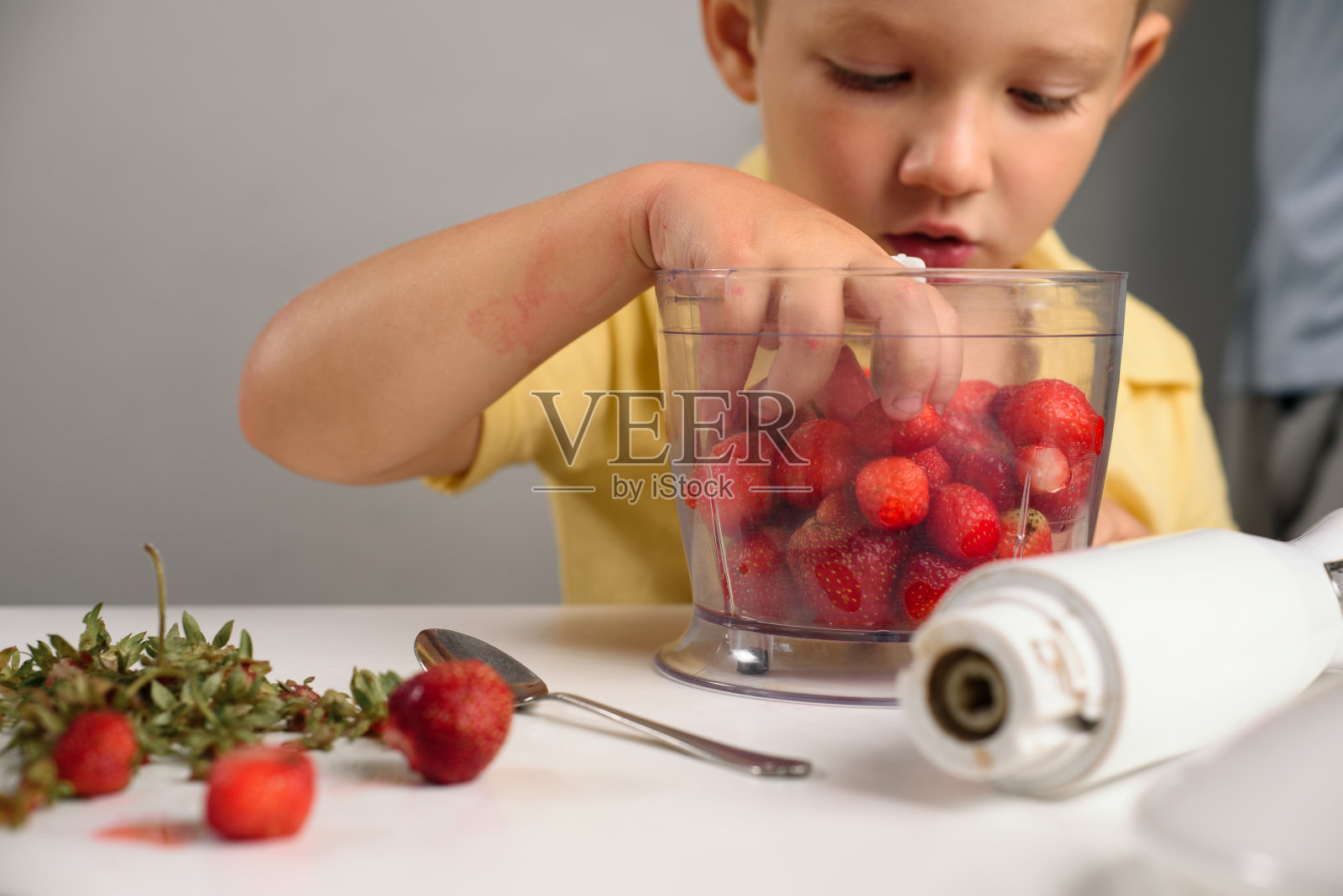 孩子把草莓放在搅拌机里搅拌。健康的食物、维生素照片摄影图片