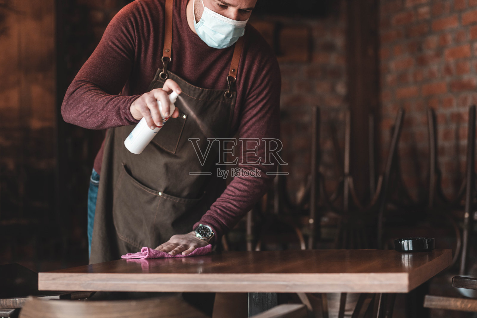年轻的服务员戴着口罩在为咖啡桌消毒照片摄影图片