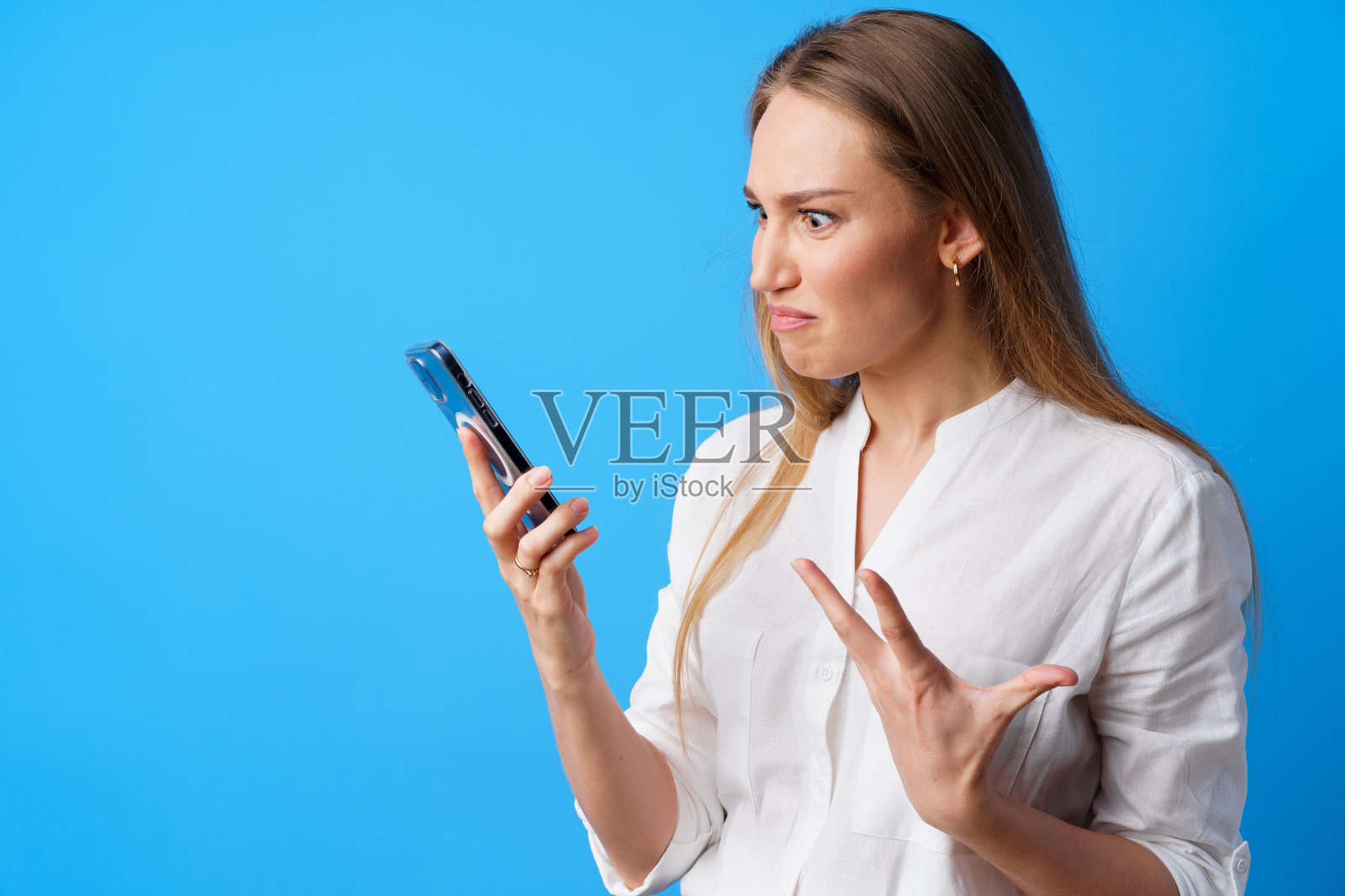 一个愤怒的年轻女人在用她的手机，生气地给别人发短信，蓝色背景照片摄影图片