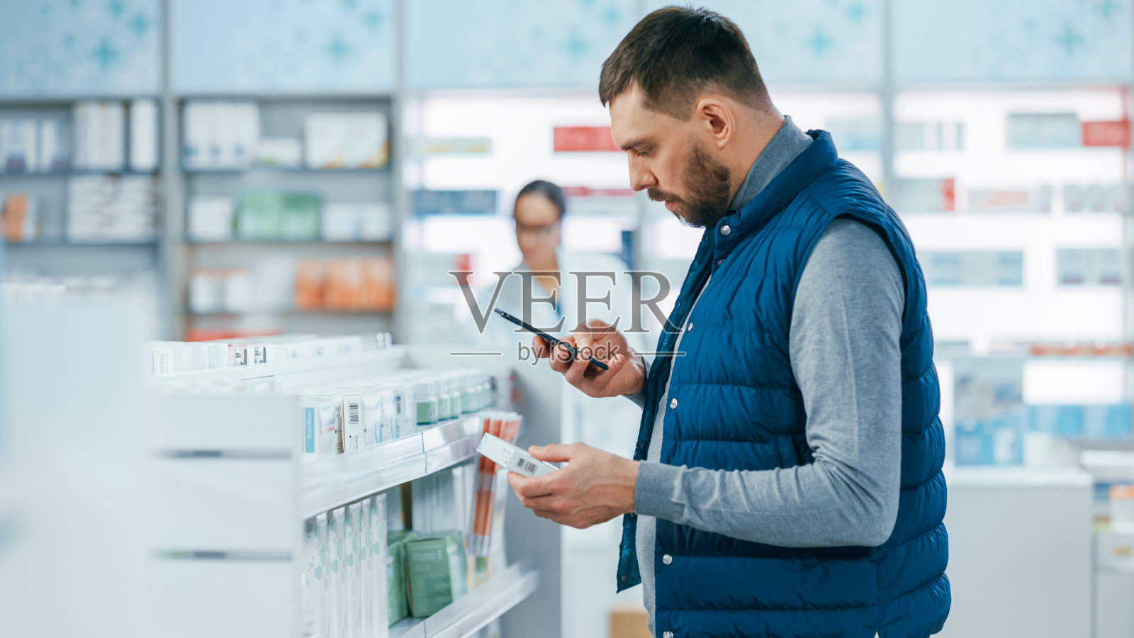 药店:英俊的年轻白人男子使用智能手机，搜索购买最好的药物，药物，维生素的肖像。货架上摆满了医疗保健，健康，运动保健品照片摄影图片