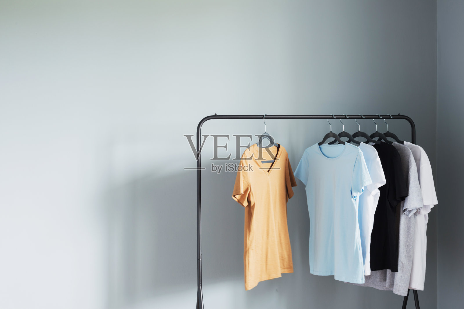 中性色的t恤挂在黑色衣架上，背靠灰色的墙壁照片摄影图片