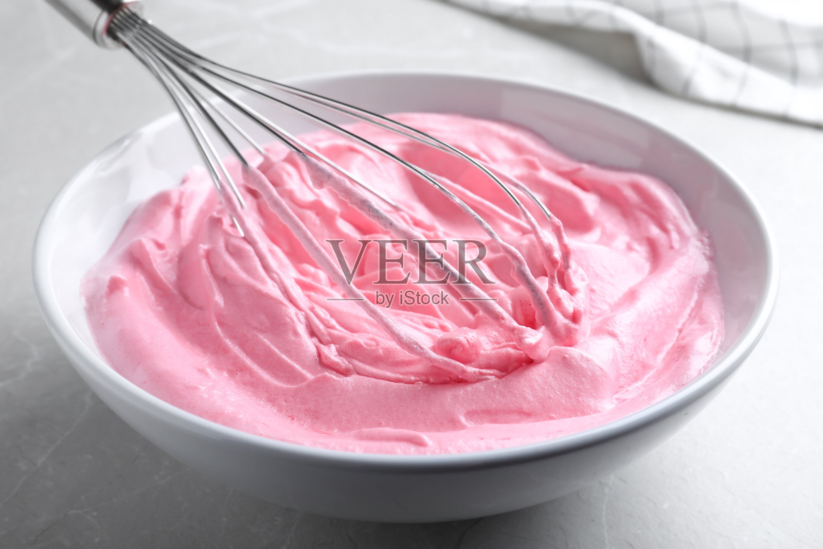 用气球打蛋器在浅灰色的桌子上搅打粉色奶油，特写照片摄影图片