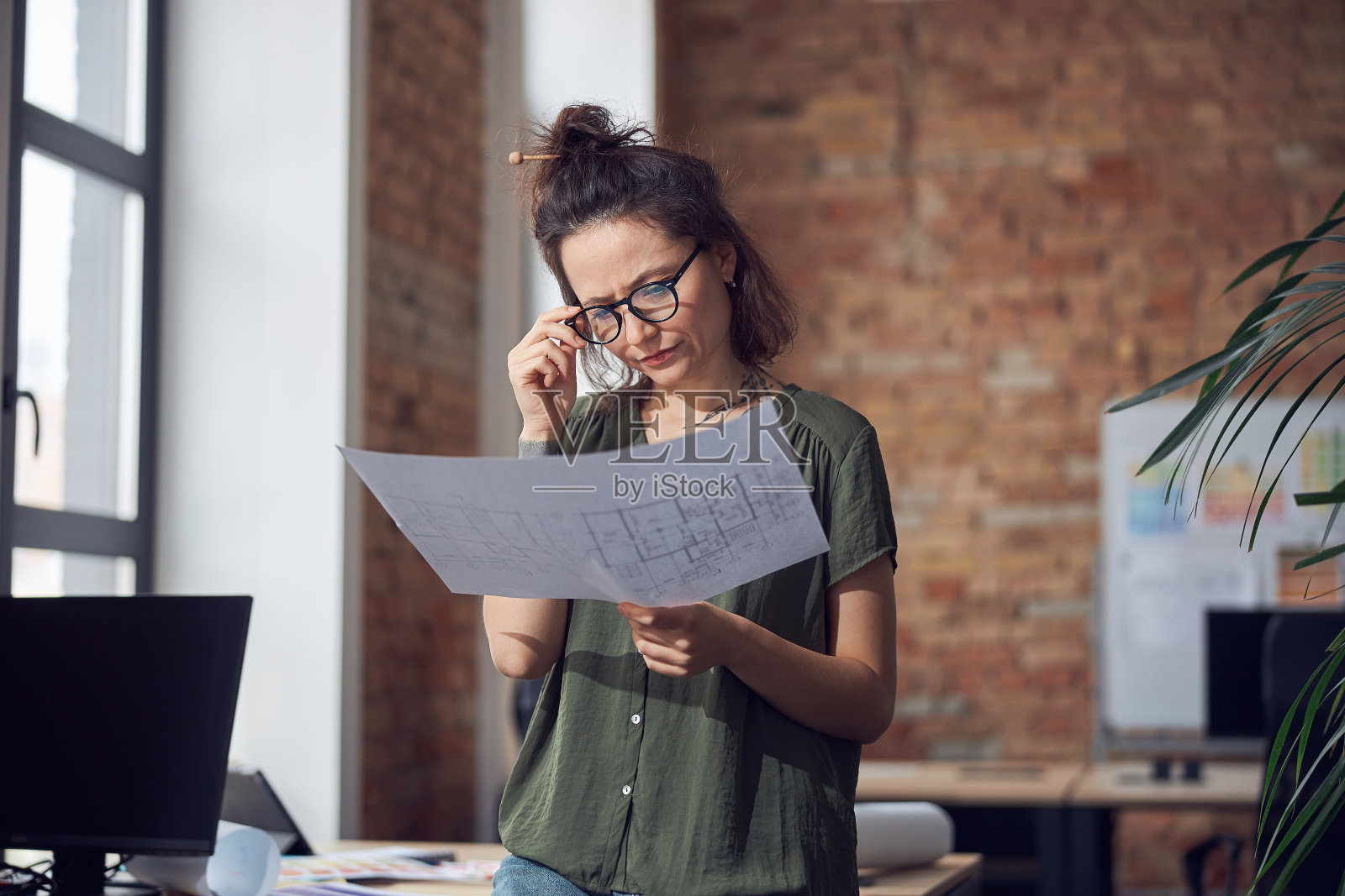 严肃的创意女性，室内设计师或建筑师戴着眼镜，专注地站在她的办公室里为新项目绘制蓝图照片摄影图片