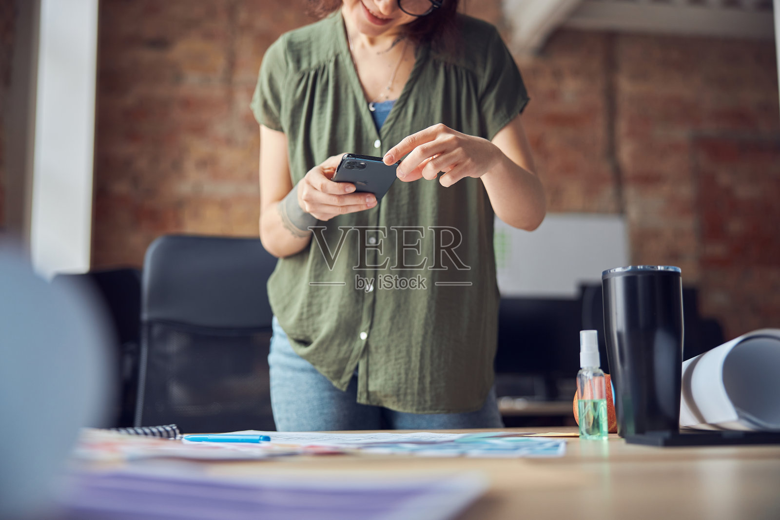 创意女性，室内设计师或建筑师，站在办公室里用智能手机发短信或拍蓝图，从事新项目。专注于手机照片摄影图片