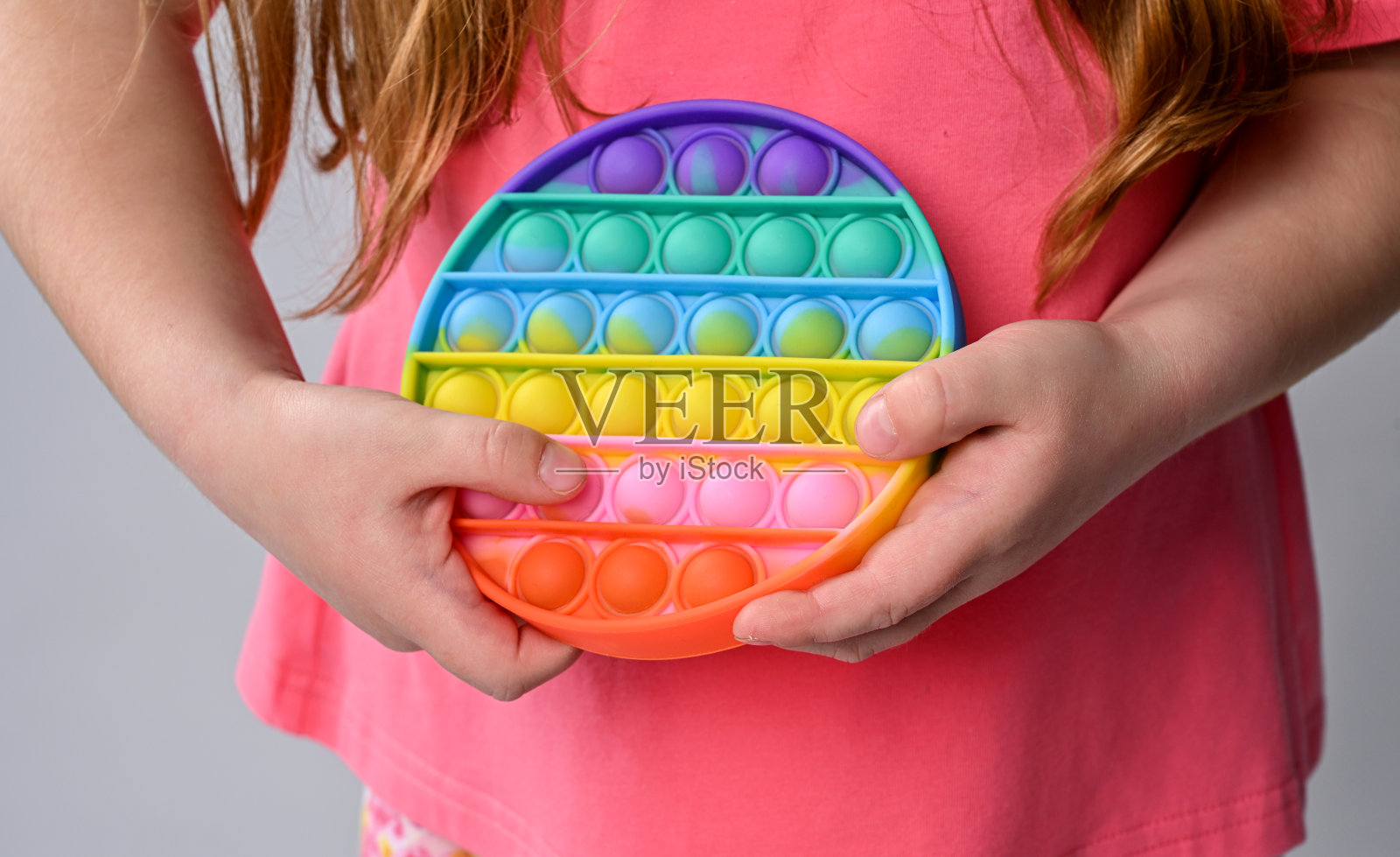 女孩手里拿着新的感官玩具-弹吧。彩虹色，凹凸气泡。硅胶的形式照片摄影图片