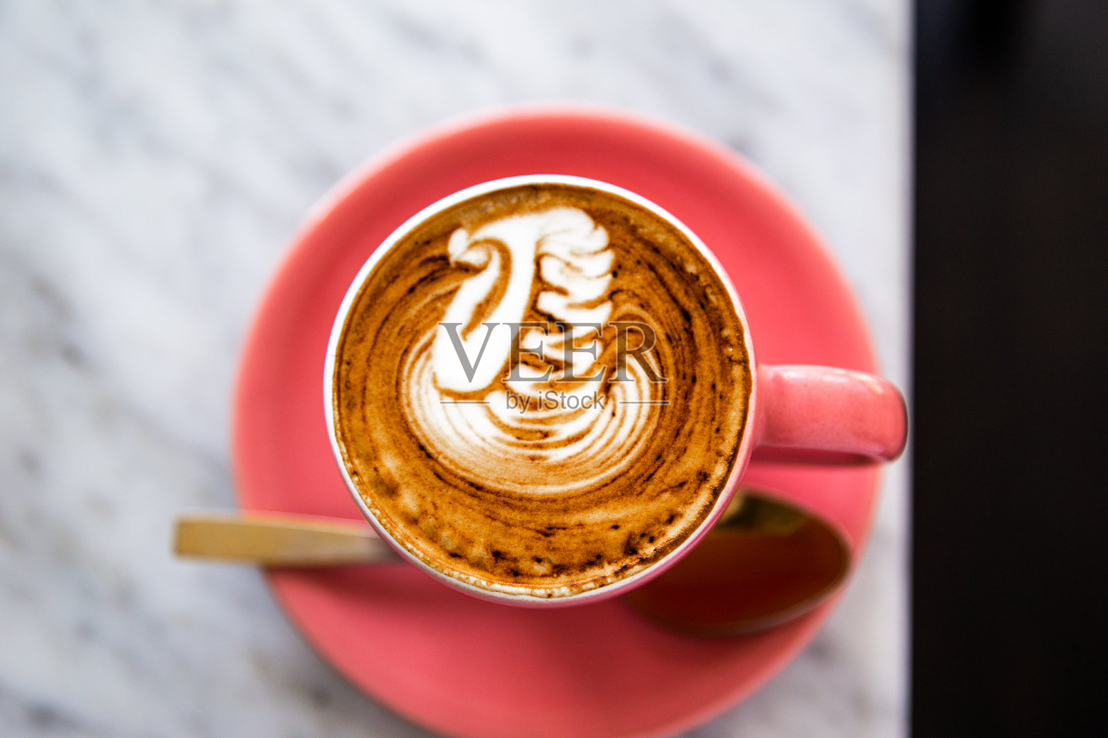 白色大理石背景上的金色调羹，粉色卡布奇诺拉花照片摄影图片