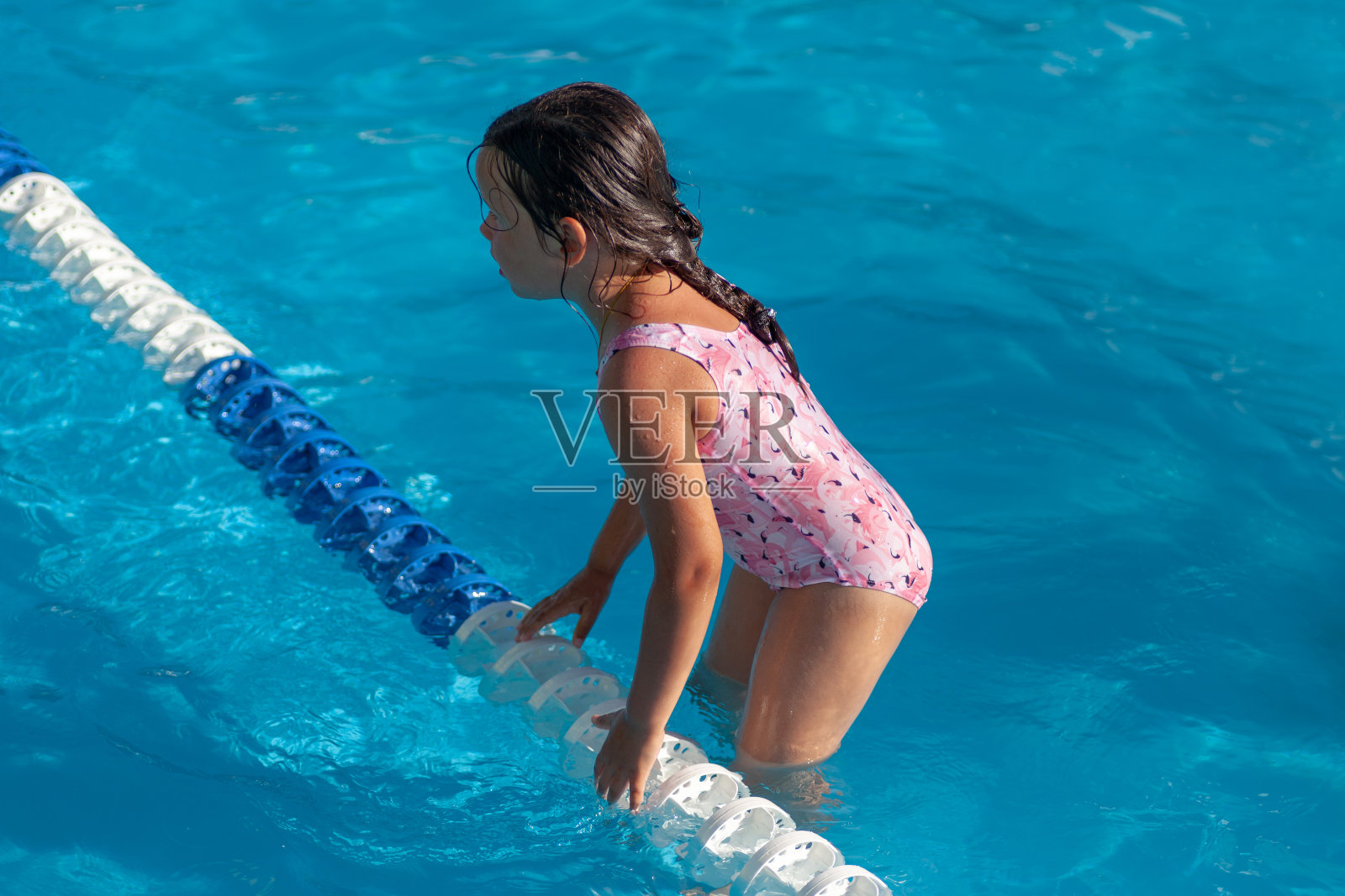 在一个炎热的夏天，一个五岁的小女孩穿着粉红色的泳衣在酒店的儿童游泳池里抓住一个塑料浮子照片摄影图片