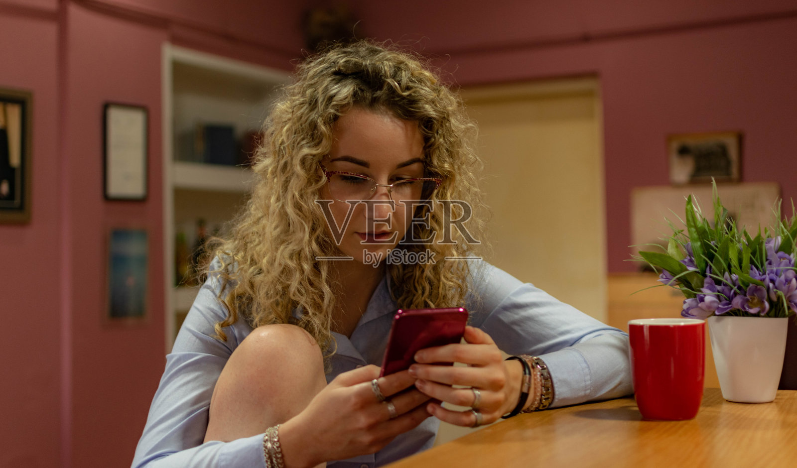 美丽的年轻女子卷发，坐在她的家，在她的阳台上，躺下，用她的智能手机与她的朋友联系，微笑着享受她的空闲时间，放松的咖啡和饼干。照片摄影图片